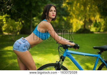 a beautiful woman is standing beside her Bicycle in the Park