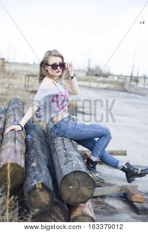 Beautiful Young Girl Sitting On Logs In An Industrial Area Of The City.