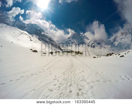 Winter landscape with sun. Experimental sun light view with snowy path and rocky peaks of Himalaya. Blue sky with fluffy clouds. Outdoor travel and extreme sport. Clean ecologic environment
