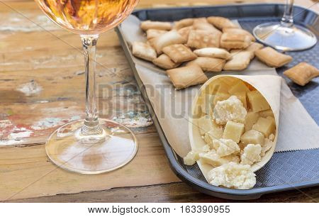 A photo of a cucurucho, a paper cone with a selection of cheeses, with a glass of wine. Market food in Spain