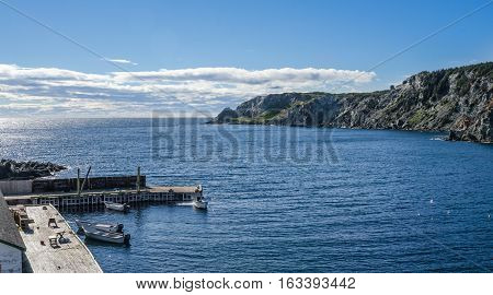 boats at a cliff-side dock house in Twillingate, Newfoundland, man works on the engine of one of 4 boats tied up to a wooden, cliff-side dock house for the day,
