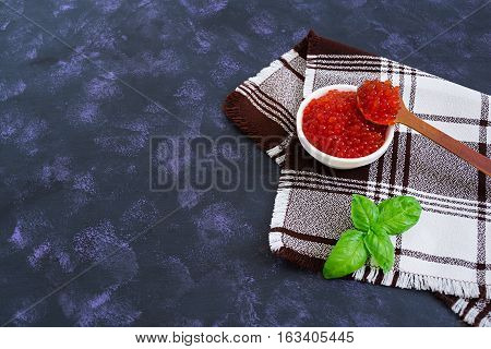 Red caviar with basil on dark background.