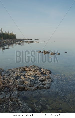 Dead calm afternoon image of clear lake huron water and limestone rocks along shoreline.