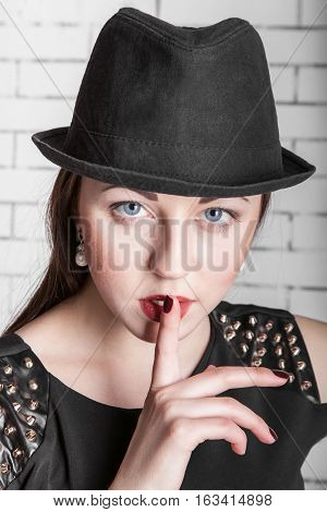 Close-up portrait of young woman in hat placing finger on lips gestures silently quiet shhhhh secret facial expression human emotions signs and symbols