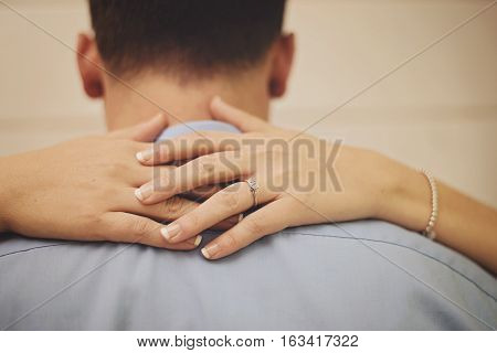 An engaged couple with the woman's hands around mans neck showing engagement ring