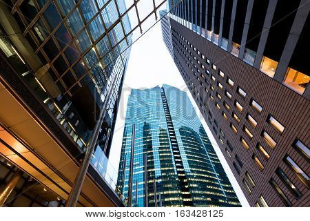 Business concept for real estate and corporate construction - looking up view in financial district the silhouettes of skyscrapers city reflect dramatic blue sky sun lights in Tokyo Japan