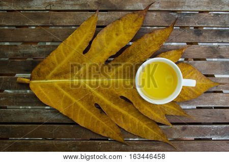 Jasmine tea cup on wooden table above yellow leaf