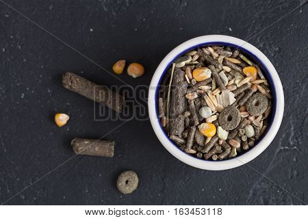 dry food for rodents in bowl on dark background top view.