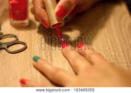 hands of a young woman who paints her nails red and green nail polish