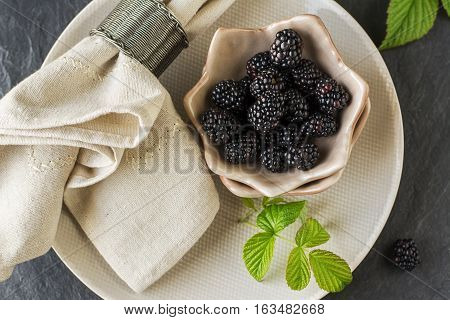 Fresh blackberries in ceramic portioned plates on a light wooden background with table linens. Top view. Style