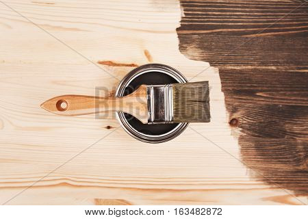 Paint brush on the can lying on wooden background. The surface is half - toned with grey color.