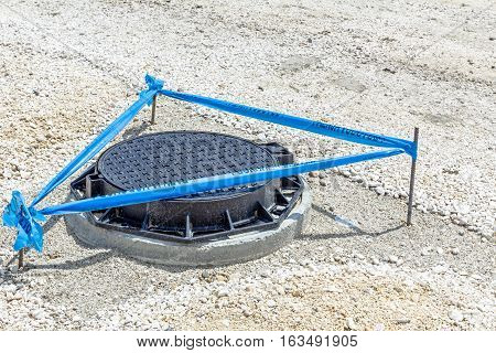 Three metal sticks with blue tape that is surrounding area around the fresh assembled new manhole with metal cover.