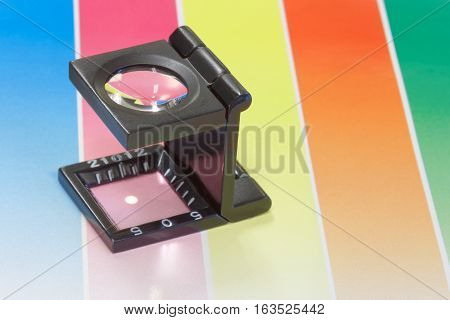 Magnifier or printer's loupe sits on a colorful CMYC test sheet in a pre-press workshop