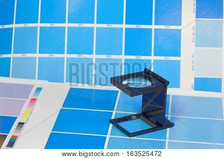 Magnifying glass standing on a leaf of the cyan test print in a pre-press workshop. Very short depth of focus