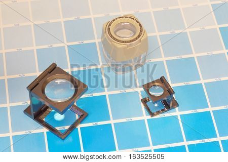 Three magnifier or printer's loupe sits on a cyan test sheet in a pre-press workshop