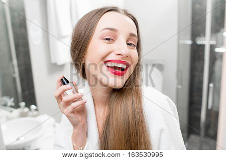 Young smiling woman spraing parfumes in the bathroom