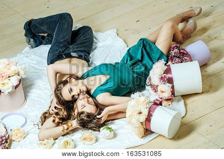 Sexy couple young beautiful cute lovers in love pretty girl and sexi man lying on back on white bedsheet among flowers on wooden floor