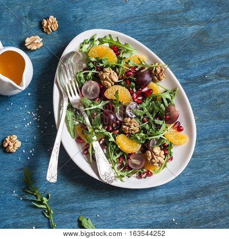 Delicious fruit salad. Grapes tangerine pomegranate and arugula fruit salad. On blue wooden background top view. Flat lay