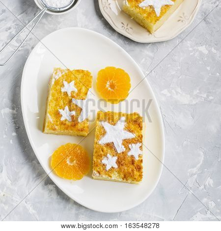 Two servings of homemade juicy mandarin biscuit with asterisks from icing sugar on a dark background. Top view