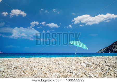 Beach umbrella on sunny Myrtos beach, the ionian sea in backgrou. Blue with white parasol on a Greek beach.