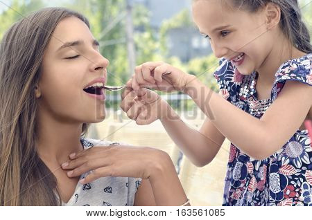 Smiling girl is feeding her sister with spoon