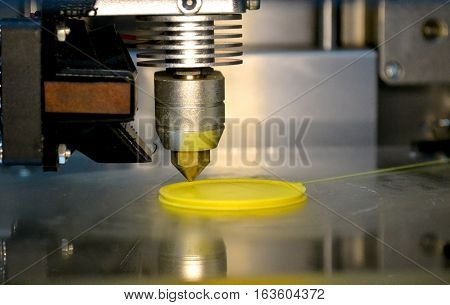 3D printer prints from the plastic figure closeup. 3D printer makes yellow model close-up on gray flat surface