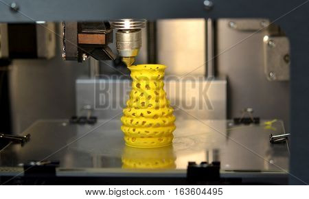 3D printer prints from the plastic figure closeup. 3D printer makes yellow model close-up on gray flat surface