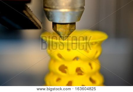 3D printer prints from the plastic figure closeup. 3D printer makes yellow model close-up on gray flat surface