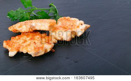 Pieces of chicken meat with edible greens on a board from slate. Close-up selective focus