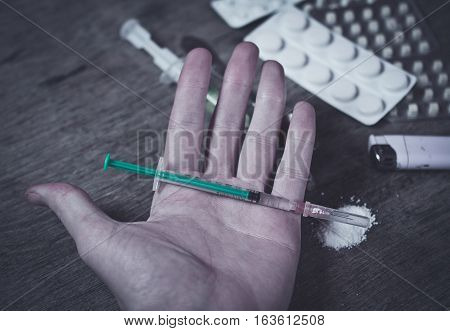 Drug Addict hand with syringe on the floor with a bag of drugs a spoon and a lighter