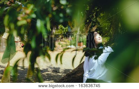 Single young Chinese woman leaning on tree trunk, smiling, on the bank of Lugu lake, Lijiang, China