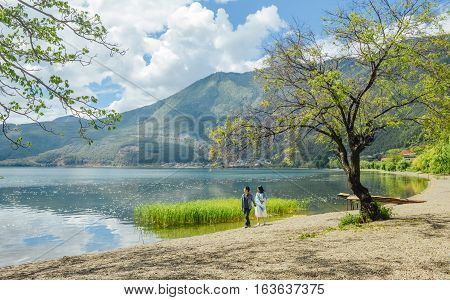 Young Chinese couple having fun while walking along the bank of Lugu lake hand in hand, at Daluoshui village, Lijiang, China