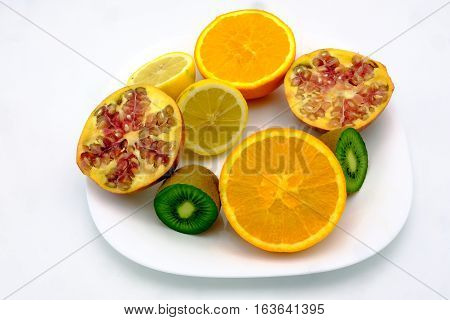 Sections of orange lemon kiwi and Pomegrenate fruits in a plate isolated on white background
