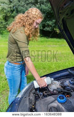 Young caucasian woman filling car cooling system with coolant in white bottle outside