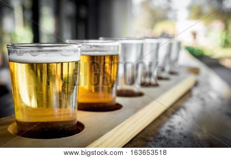 Beer samplers in small glasses individually placed in holes fashioned into a unique wooden tray. Focus is on the backlit front sample.