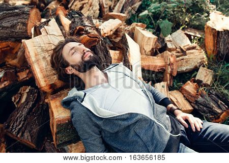 Tired lumberjack sleeping on pile of wood. Exhausted woodcutter having rest after hard work. Masculinity, manhood, handiwork, strength concept