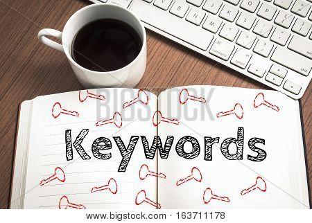 Keywords written on notebook keyboard and coffee on wood table