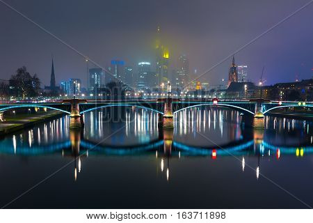 Picturesque view of Frankfurt am Main skyline and Ignatz Bubis Brucke bridge during evening blue hour with mirror reflections in the river, Germany