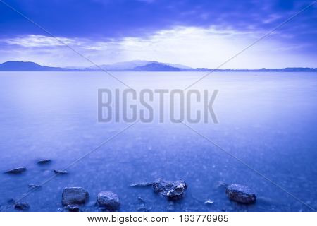 Sunset Lake. On a background the mountains. Tops of stones in water. Play of light and shadow creates a gorgeous volume and distance. Long exposure.