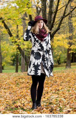 Woman in a floral patterned coat and wine red hat in the park. Happy girl and colorful autumn forest. Portrait of a lady yellow green red and brown leaves background