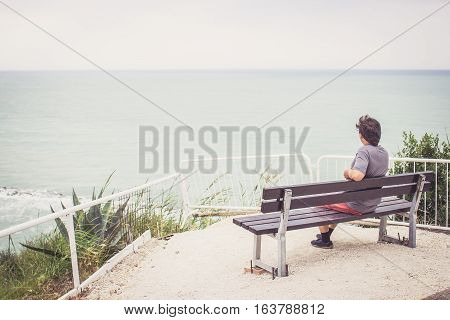 Young Man Sitting On Bench Overlooking Sea