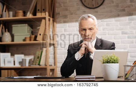 Some issues must be taken care of. Professional doubtful mature manager sitting at his desk and trying putting some thought into important problems