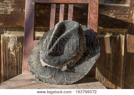 Battered old hat damaged by clothes moth on vintage background. A forgotten hat covered with spider web among the ruins of a house. Imagine the owner of this hat and tell their story.