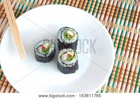 Three portions of sushi rolls with ingredients lies on white plate on wicker kitchen tablecloths. Photo closeup