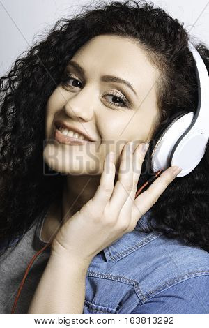 Everything is cool. Satisficed girl correcting earphones, making-up good, smiling and feeling calmness, light background