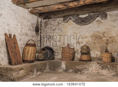 Basement of an old house with wooden beams and wall with humidity, antique household items, carboy demijohn, stewpot, plank, Wicker basket, pulley with chain, yuguillo