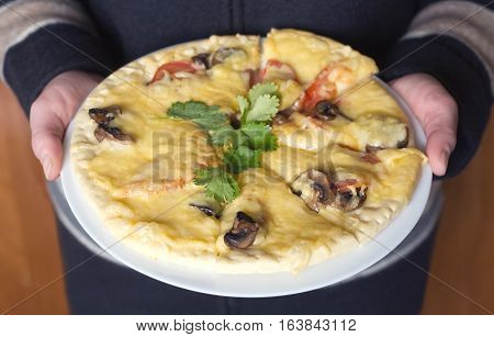 Woman in strips cloths holds large white plate delicious pizza with mushrooms tomatoes and parsley. Photo closeup