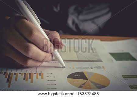 Close up business man hand holding pen pointing stock market document in office on the wood desk.