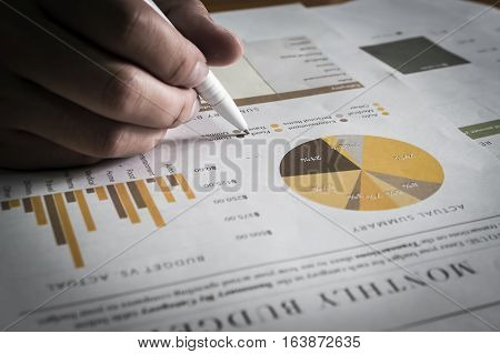 hand holding pen pointing stock market document for analysis document in office.