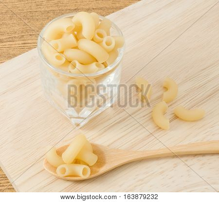 Food and Cuisine Uncooked Elbow Macaroni or Gomiti Pasta in A Wooden Spoon on Cutting Board.